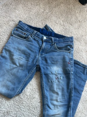 Blå jeans från Levi's - Ett par klassiska blå jeans från Levi's med fem fickor och slitna detaljer på framsidan. Jeansen har en rak passform och är tillverkade i denim med en snygg tvättad look. Perfekta för en avslappnad och trendig stil.