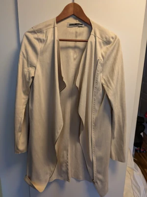 Beige  kappa från Noisy May - Stilren beige kappa från Noisy May i storlek S. Kappan har öppen front utan knäppning, långa ärmar och en mjuk, slät yta. Perfekt för lager-på-lager och ger en clean look till din outfit.