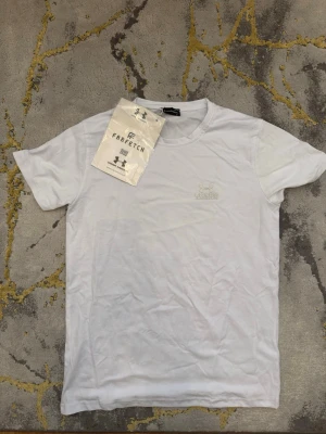 Vit t-shirt från Under Armour - Vit t-shirt från Under Armour med klassisk rund hals och diskret logga på bröstet. Enkel och stilren design som passar till det mesta. Tillverkad i mjuk bomull för en skön känsla hela dagen.
