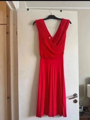 LA short dress från Jessica Frej - Snygg röd långklänning från Jessica Frej, LA short dress, med omlottliv och djup v-ringning. Klänningen har ett elegant fall och är ärmlös, perfekt för dig som vill sticka ut. Tillverkad i ett mjukt och följsamt material som ger en lyxig känsla. Använt vid 2 tillfällen. 