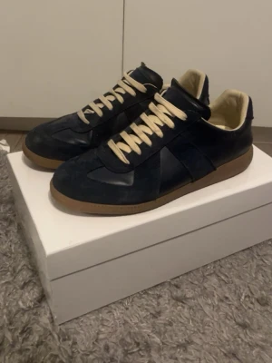 Mörkblå sneakers med beige sula - Snygga mörkblå sneakers med beige snörning och kontrasterande gummisula i brunt. Ovandelen är i mocka och läder för en stilren look. Insidan är ljus och skön, perfekt för dig som gillar klassiska men trendiga skor.