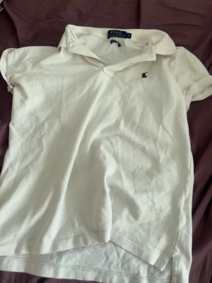 Vit pikétröja från Polo Ralph Lauren - Klassisk vit pikétröja från Polo Ralph Lauren i modellen The Skinny. Tröjan har korta ärmar, krage och liten blå broderad logga på bröstet. Storleken står M men passar även S. Har små svettfläck men går nog bort med fläckborttagning.