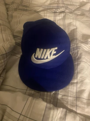 Blå Nike keps med broderad logga - Snygg blå keps från Nike med stor vit broderad logga framtill. Klassisk snapback-modell med platt skärm och justerbar baksida. Tillverkad i bomullsmix för skön passform. Perfekt accessoar för en sportig och trendig look.