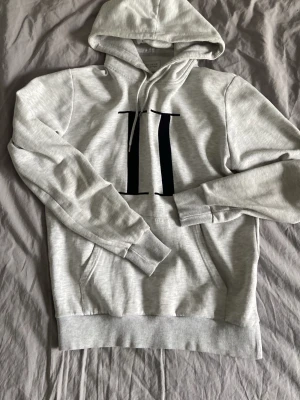 Les Deux Hoodie - Snygg ljusgrå hoodie från Les Deux med stor svart logga på bröstet. Klassisk modell med huva och dragsko samt känguruficka framtill. Perfekt för en avslappnad och trendig stil. Storlek L men passar som M.
