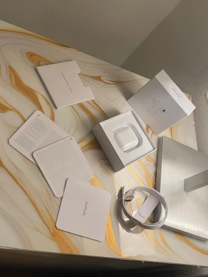 Apple AirPods med laddningsetui - Säljer ett par vita Apple AirPods med laddningsetui. Trådlösa hörlurar i stilren design, tillverkade i blank plast. Kommer med originalförpackning, laddningskabel och manualer. Perfekta för musik, samtal och vardagsbruk.