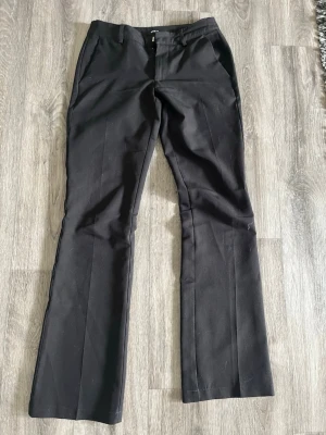 Svarta kostymbyxor med pressveck - Snygga svarta kostymbyxor med pressveck och raka ben. Byxorna har fickor fram och passpoalfickor bak. Klassisk midja och stängs med knapp och dragkedja. Perfekta för en stilren look och passar till många olika outfits.