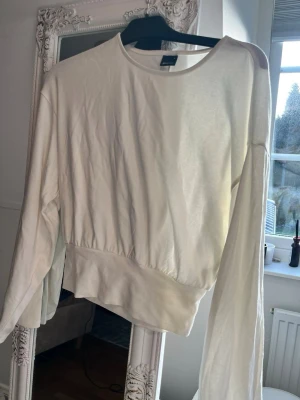 Vit långärmad topp från Gina Tricot - En enkel och stilren vit långärmad topp från Gina Tricot. Modellen har rund halsringning och bredare resår i midjan för en snygg passform. Perfekt att matcha med jeans eller kjol för en clean look.