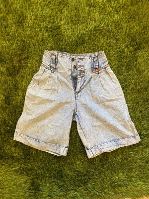 Lee Vintage Högmidjade ljusa baggy denimshorts - Säljer ett par vintage högmidjade ljusa denimshorts från Lee med knappstängning och baggy fit. Shortsen har fickor fram och har en väldigt retro look.