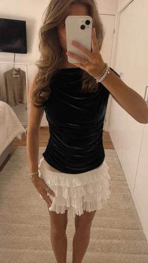 Svart sammetsärmlös topp - Snygg svart topp i sammet med ärmlös design och draperad effekt. Toppen har en elegant, figurnära passform och hög halsringning. Perfekt att styla med kjol eller jeans för en trendig look.