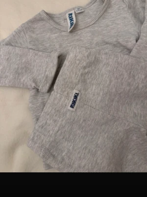 Grått ribbat set från RIKIKI - Supermjuk och ribbad pyjamas från RIKIKI i ljusgrått. Setet består av långärmad tröja och byxa, perfekt för mysiga nätter. Materialet är stretchigt och bekvämt för de allra minsta.