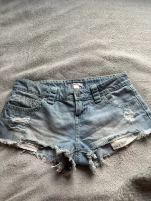 Ljusblå jeansshorts med fransar - Säljer ett par ljusblå jeansshorts med slitna detaljer och fransig kant. Shortsen är märka i S men enligt mig är dem stora i storleken så jag skulle säga runt S/M