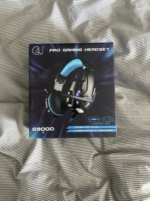C4U G9000 Pro Gaming Headset - Gamingheadset från C4U, modell G9000, med svart och blå design. Over-ear-modell med vadderad bygel och mikrofon. Ansluts via USB eller 3,5 mm-kontakt och är kompatibel med laptop, PC, mobil och tablet. Inkluderar adapter för extra kompatibilitet.