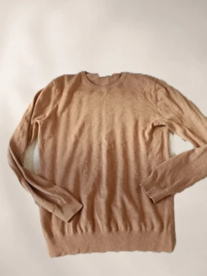 Beige stickad tröja från Bläck - Snygg beige stickad tröja från Bläck med rund halsringning och långa ärmar. Tröjan har en enkel och stilren design med ribbade muddar vid ärmslut och nederkant. Perfekt att matcha med jeans eller kjol för en clean look.
