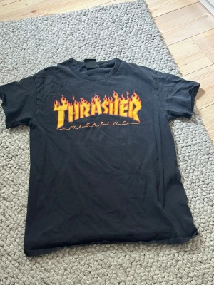 Svart Thrasher t-shirt med flames - Trasher skateboard magazine t shirt som köptes för 500kr tidigare i år har såklart används men bra skick inga fläckar eller hål det finns ingen storlek på tröjan men måtten är  Längd: 61–62 cm Bredd: 40–41 cm Axelbredd: 33–34 cm  Priset är inte hugget i sten 😊  (Obs skriver XS i annonsen då inget annat finns).