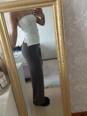 Vit bandeau tubtopp med slits - Säljer en vit bandeau tubtopp som är axelbandslös och har slits på sidorna. Toppen har en clean och enkel design med rak passform och är perfekt för dig som gillar minimalistisk stil. Materialet känns mjukt och lätt. Storlek M, men passar även S