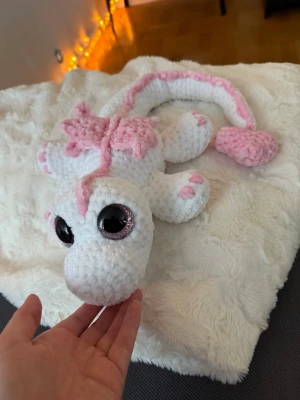 Vit drake med rosa detlajer:) - Denna urgulliga drake är en en vit drake med rosa detaljer, virkat med mjukt garn från Rusta som heter Klara🫶🏼 Den har hårda rosa ögon som inte går att ta av, sitter som bergen🩷✨ Den är cirka 54 cm lång🩷