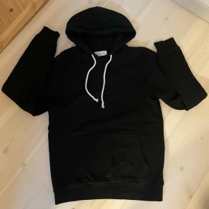 HOODIE | PIER ONE. - En stilren svart hoodie med klassisk känguruficka och vit dragsko i huvan. Hoodien har ribbade muddar vid ärmslut och nederkant. Perfekt för en avslappnad och trendig look.
