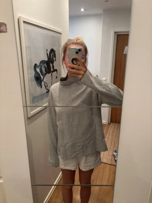 Ljusgrå oversized tröja med hög krage - Ljusgrå oversized tröja med hög krage och långa ärmar. Tröjan har en avslappnad passform och är tillverkad i ett mjukt material som känns skönt mot huden. Perfekt för en chill och stilren look.