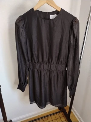 Två blusar i svart och blått - Säljer två blusar, en svart med puffärm och markerad midja samt en blå transparent blus med lös passform. Båda har rund halsringning och långa ärmar. Perfekta för dig som gillar stilrena och trendiga plagg.