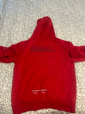 Röd hoodie från Hoodrich - Cool röd hoodie från Hoodrich med svart logotyp på bröstet och detaljer på ärmen. Hoodien har en stor huva och en praktisk magficka. Materialet är mjukt och bekvämt, perfekt för att chilla eller hänga med kompisar. Insidan av huvan är grå för en snygg kontrast.