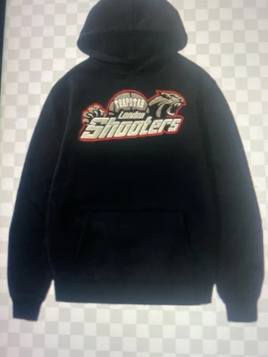 Trapstar London Shooters hoodie svart - Svart hoodie från Trapstar med stor broderad 'London Shooters'-logga och pantermotiv på bröstet. Klassisk känguruficka framtill, ribbade muddar och justerbar huva med snören. Perfekt för dig som gillar streetwear och vill sticka ut.