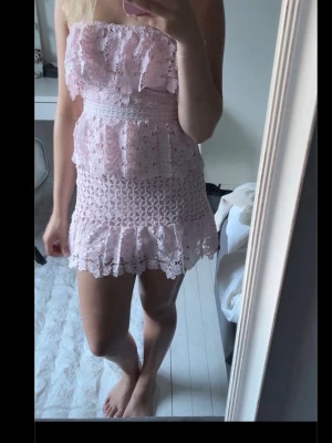 Ljusrosa spetsklänning med volanger - Söt kort klänning i ljusrosa spets med volangdetaljer. Säljer vidare, var bara använd en gång innnan! 