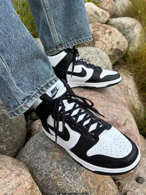 Nike Dunk High Panda sneakers - Nike Dunk High sneakers i svart och vitt läder med klassisk Swoosh på sidan. Högt skaft, svart snörning och perforerad tåbox för extra ventilation. Tidlös och clean design som passar till jeans eller streetwear.