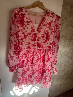 Blommig kortklänning från ONLY - Supersöt kortklänning från ONLY i vitt och rosa med blommigt mönster. Klänningen har v-ringning, långa ärmar och volangdetaljer i kjolen. Perfekt för sommarens alla tillfällen och ger en fräsch och romantisk look.