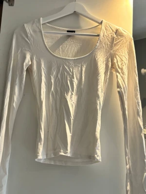 Vit långärmad topp med rund hals - En enkel och stilren vit långärmad topp med rundad halsringning och utsvängda armar. Perfekt att matcha med jeans eller kjol för en clean look.