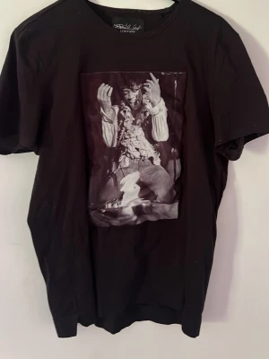 Svart t-shirt med fototryck från Limitato - Svart t-shirt från Limitato med ett stort svartvitt fototryck på framsidan. Klassisk rund hals och korta ärmar. T-shirten har en avslappnad passform och är tillverkad i mjuk bomull som känns skön mot huden. Perfekt för dig som gillar statement-plagg.