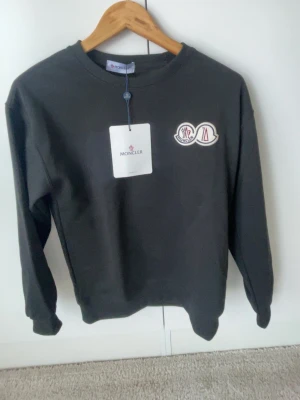 Svart sweatshirt från Moncler - Snygg svart sweatshirt från Moncler med rund halsringning och Moncler-logga på bröstet. Tröjam passar en som bär storlek XS då den sitter tight. 