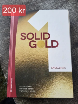 Solid Gold 1 Engelska 5 kursbok - Solid Gold 1 är en kursbok i engelska för gymnasiet, Engelska 5. Boken har hårda pärmar med röd rygg och framsida i vitt och guld. Författare är Eva Hedencrona, Karin Smed-Gerdin och Peter Watcyn-Jones. Perfekt för dig som pluggar engelska på gymnasiet.