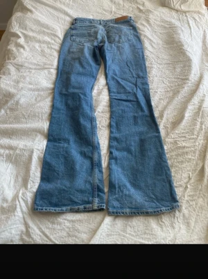 Ljusblå utsvängda jeans - Säljer ett par ljusblå jeans med utsvängda ben och klassisk femficksmodell. Jeansen har hög midja och är tillverkade i denim med en snygg tvätt. Perfekta för dig som gillar retrostil och vill ha ett par riktigt schyssta jeans med mycket karaktär.
