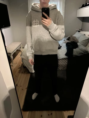 Grå hoodie med broderad logga från Bvaldi - Snygg grå hoodie med stor huva och ribbade muddar. På bröstet och ärmen finns en vit broderad logga som ger en clean och modern look. Hoodien är i mjukt material, perfekt för chill dagar. Passar till det mesta och är enkel att matcha. 