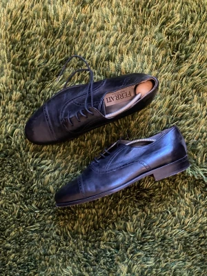 Svarta läder loafers från Ferrati - Snygga svarta loafers från Ferrati i äkta läder med klassisk snörning och låg klack. Skorna har en elegant, spetsig tå och diskreta sömdetaljer. Passar bra till fina middagar, bröllop och andra festligheter.
