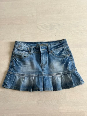 Blå jeanskjol med volangkant - Snygg blå vintage jeanskjol från Lonky med volangkant nedtill och klassiska fickor fram och bak. Storlek 26-passar typ xxs-s