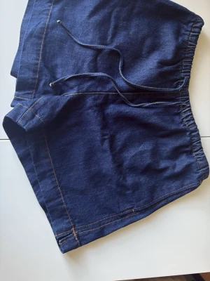 Mörkblå denimshorts med snörning - Snygga mörkblå shorts i denim-look med elastisk midja och snörning framtill. Fickor på sidorna.