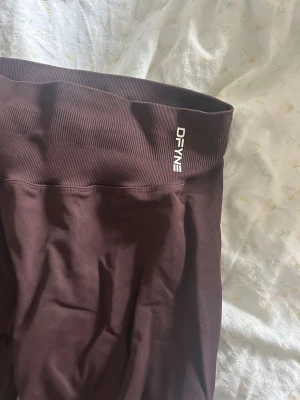 Bruna impact leggings från DFYNE - Intressekoll på mina DFYNE impact  i storlek small. De har mellan hög midja och är tillverkade i ett stretchigt material av 90% nylon och 10% elastan. Perfekta för träning eller chill dagar. Snygg logga på linningen. Längd tall. Använt en gång.