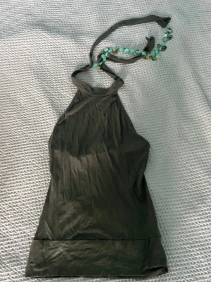 Vintage Mörkgrön halterneck topp - Snygg mörkgrön halterneck linnetopp med knyt i nacken. Toppen har en enkel, stilren design och är ärmlös, vilket gör den perfekt för varma dagar. Materialet känns mjukt och lätt mot huden.