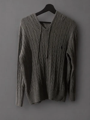 Grå stickad hoodie från Ralph Lauren - Snygg grå stickad hoodie från Ralph Lauren med kabelstickat mönster och broderad logga på bröstet. Storlek S, helt i nytt skick och pris kan diskuteras.