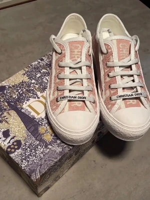 walk n dior platform sneaker - Snygga sneakers från Dior med rosa och vit monogramdesign. Skorna har vita snören, gummisula med stjärndetalj undertill och tydlig Christian Dior-logga på sidan. Ovandelen är i textil och sulan är i kraftigt vitt gummi. Perfekta för dig som vill sticka ut med lyxig streetstyle.