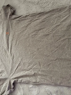 Beige t-shirt från Les Deux - Snygg beige t-shirt från Les Deux med diskret broderad logga på bröstet. Klassisk rund halsringning och korta ärmar. Tillverkad i mjuk bomull som känns skön mot huden. Perfekt basplagg för en clean och enkel stil.