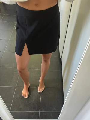 Svart kortkjol med slits - Svart kortkjol med slits framtill. Kjolen är högmidjad och i italiensk storlek 42, jag skulle säga att den passar mig som vanligtvis är en 34/XS då den är lite tajtare i midjan. Märket heter United colors of Benetton💕