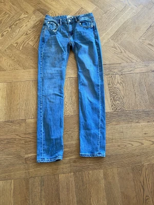 Blå raka jeans från 157 - Säljer ett par klassiska blå jeans från 157 i rak modell. Jeansen har fem fickor, knappgylf och kontrastsömmar. Perfekta till vardagsstilen och tillverkade i slitstarkt denimtyg. Passar dig som gillar enkel och tidlös look.
