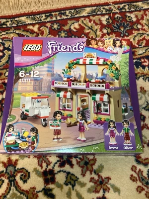 LEGO Friends Pizzeriaset 41311 - Säljer ett LEGO Friends set, modell 41311, som föreställer en färgglad pizzeria med tillbehör och figurerna Emma och Oliver. Setet har detaljer som pizzaugn, scooter och pizzakartonger. Perfekt för dig som gillar att bygga och leka med LEGO Friends.