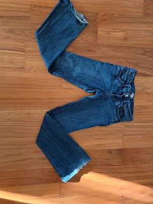 Mörkblåa bootcut jeans från Gina - Säljer ett par klassiska blå jeans med bootcut passform. Jeansen har fickor, knappgylf och en snygg tvättad look. Perfekta till vardagsstilen och passar till det mesta. Materialet är denim i bomull.