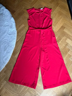 Croppad hallonröd jumpsuit - Superfin hallonröd jumpsuit i croppad culottemodell. Innerbenslängd 56 cm. Minimala noppor längst ner på insidan benen, se bild. Syns bara om man är riktigt nära. 