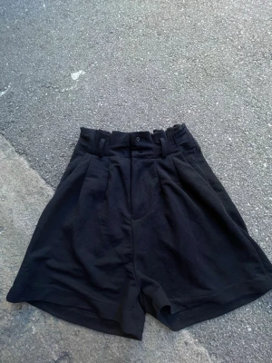 Svarta högmidjade shorts från BikBok - Säljer ett par svarta högmidjade shorts från BikBok. De har breda hällor, knapp och dragkedja framtill samt en lös passform i benen. Perfekta till sommaren och lätta att matcha med olika toppar.