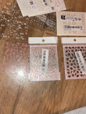 Mixade nagelstickers blommor & stjärnor - Säljer flera ark nagelstickers med olika motiv som blommor, stjärnor, fjärilar och snöflingor. Motiven är i färger som rosa, guld, svart och silver. Perfekt för att skapa unika nageldesigner hemma. Materialet är tunt plastfilm som enkelt fästs på nageln.
