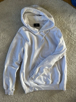 Vit hoodie från H&M - Säljer en klassisk vit hoodie från H&M med huva. Hoodien har en stor magficka och ribbade muddar vid ärmslut och nederkant. Perfekt för en chill och avslappnad stil. Tillverkad i mjukt bomullsmaterial. Är lite nopprig men inget man tänker på. Lite mindre i storleken 